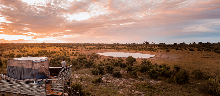 A guest enjoying sunrise views over the Khwai Reserve waterhole from their elevated Skybed.