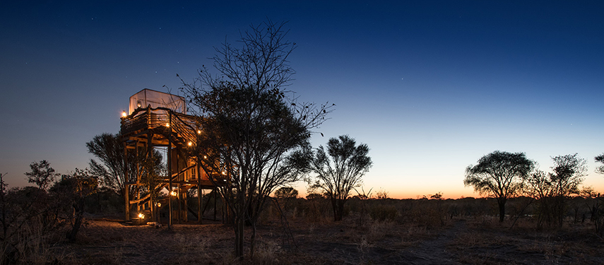 Skybed platform aglow with warm lights beneath a twilight sky in the Khwai Private Reserve.