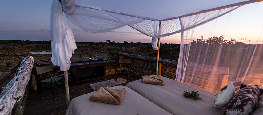 Twin open-air beds draped in mosquito netting on a Skybeds platform at dusk.