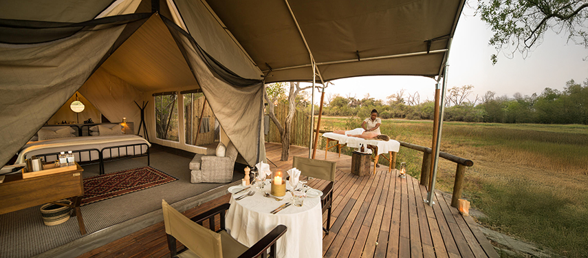 A private deck at Little Machaba with spa treatment set-up and a table set for two, facing out over the open bush.