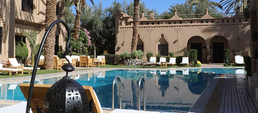 Shimmering turquoise swimming pool framed by palm trees and kasbah walls at Ksar El Kabbaba.