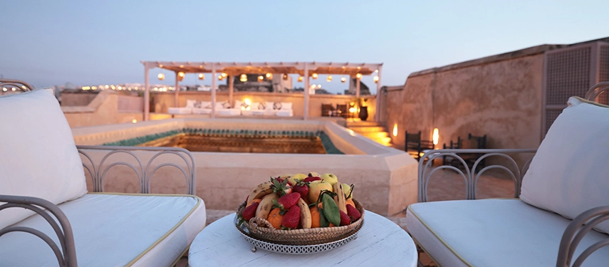 Evening rooftop setting at Dar Bensouda with a fruit platter, pool, and lantern-lit seating area.