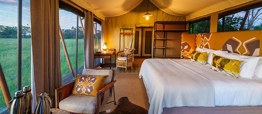 A spacious tented bedroom opens to wraparound views of the grasslands with warm natural light filling the interior.