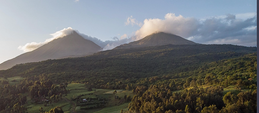 Panoramic view of the Virunga volcanoes with dense forest and scattered farmland below.