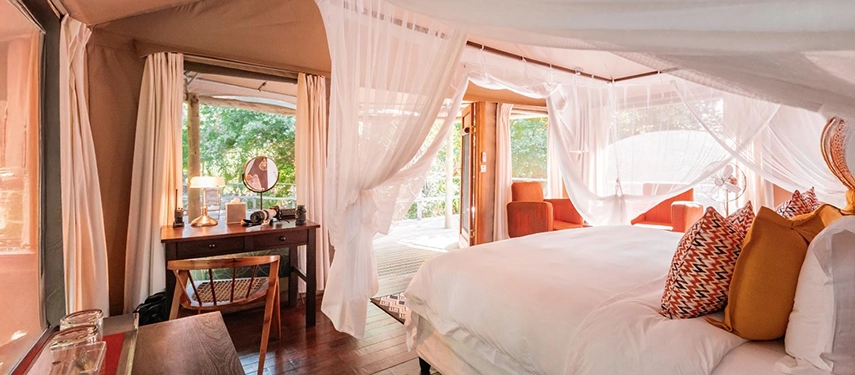 A spacious tented bedroom with a canopied bed, writing desk and gauzy netting opens onto a shaded deck overlooking Gorongosa’s forest.