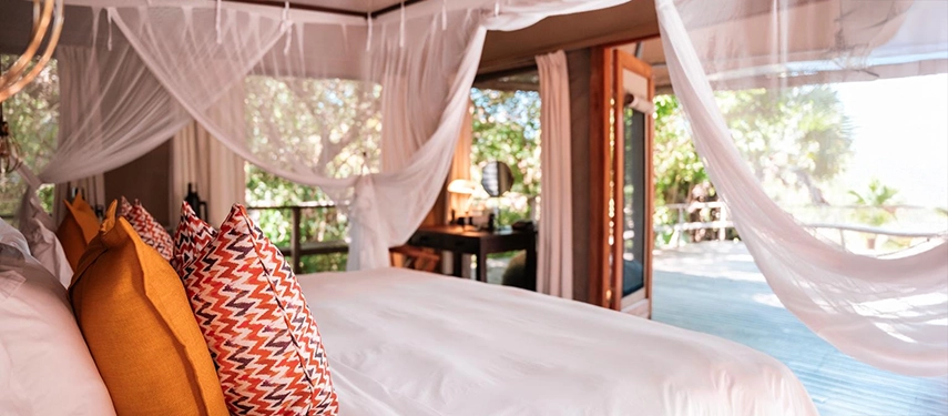 Inside a tented suite, a soft white bed draped with mosquito netting opens onto a shaded deck overlooking the forest.