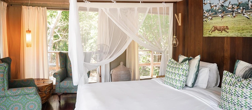 Soft natural light fills a tented suite with patterned cushions, wooden floors and leafy views through wide windows.