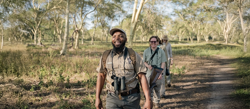 A smiling walking safari guide leads guests through open woodland, capturing the warmth, expertise and intimacy of Gorongosa’s on-foot experiences.