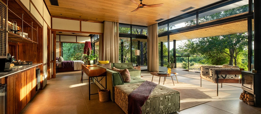 Spacious suite interior with a comfortable lounge area, mini-bar, and glass walls opening to the outdoors.