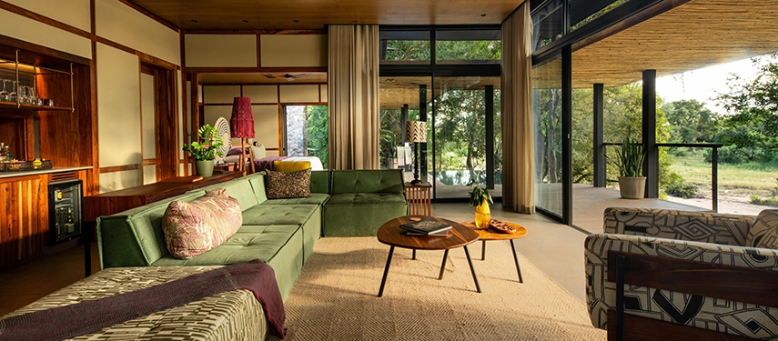 A cozy corner of the suite featuring a large green L-shaped sofa, wooden coffee tables, and views of the bush.