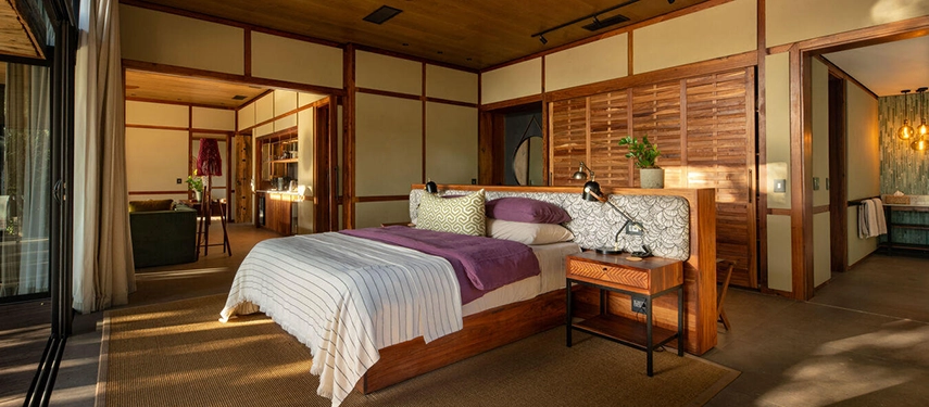 The bedroom area of a suite with a king-sized bed, purple throw pillows, and wooden sliding doors.