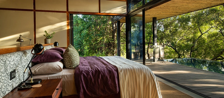 A side view of the bedroom opening directly onto the private deck and plunge pool with lush green trees outside.