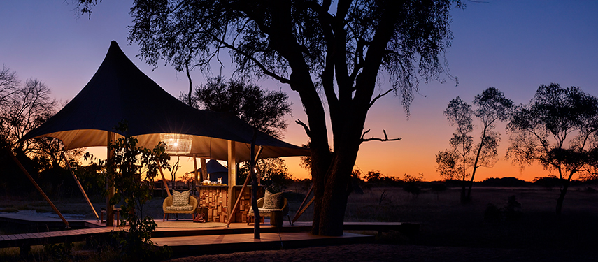 Atmospheric entrance area at Tuludi Camp lit by chandeliers and lanterns, set beneath a dramatic tented roof at twilight.