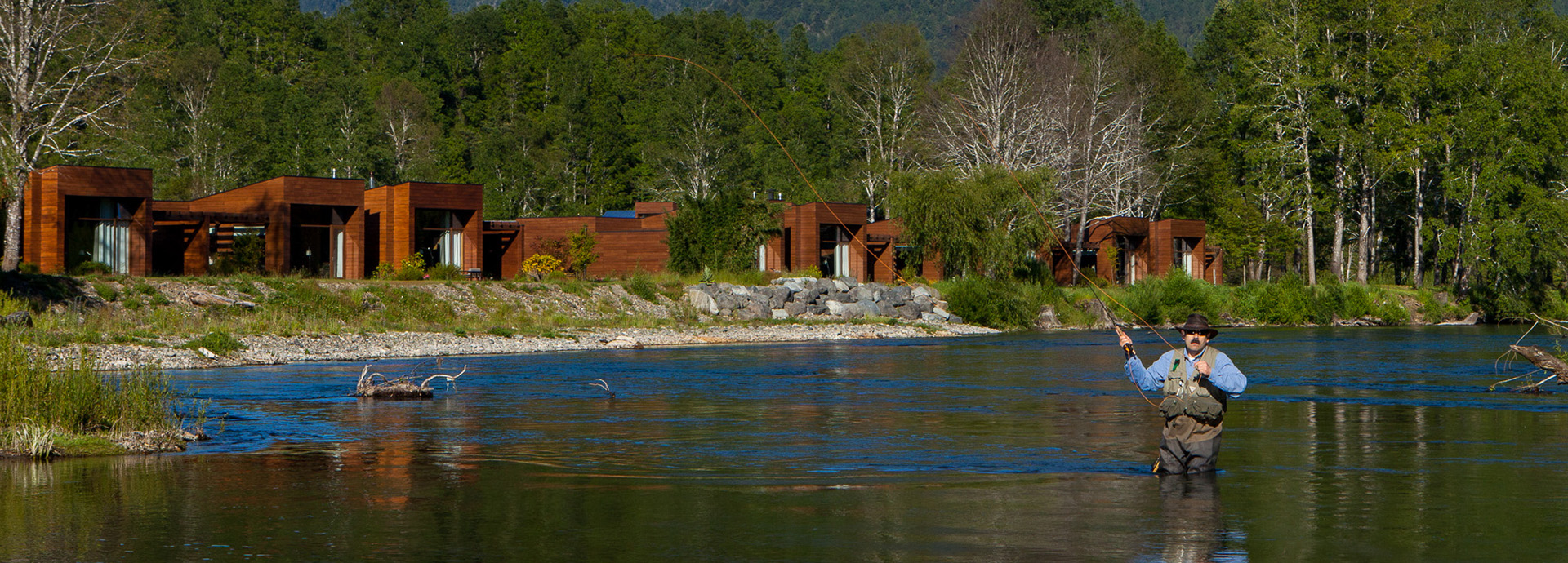 Tourist fly fishing on Liucura River in Chile's Lake District with snowcapped mountains in the background