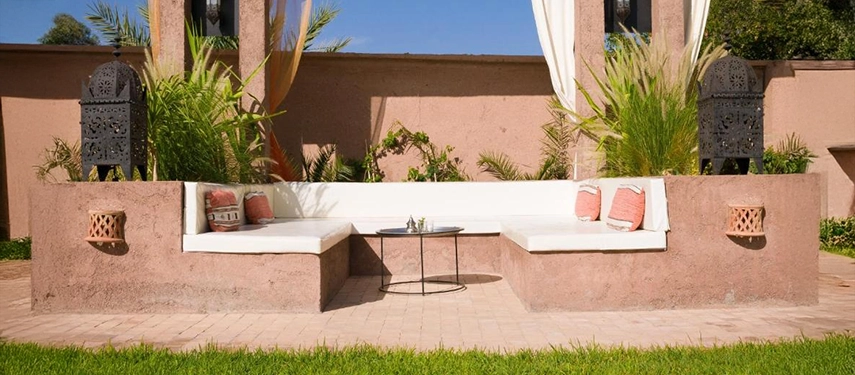Cozy garden alcove with white cushioned seating, decorative lanterns, and a small tea table.
