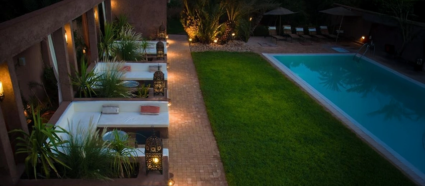 Evening view of lantern-lit garden alcoves beside the pool with lush greenery.