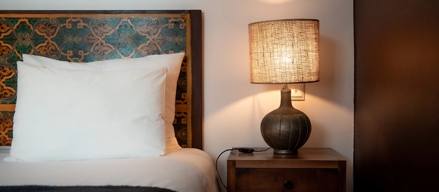 Close-up of a bedside table with a rustic lamp and decorative patterned headboard.