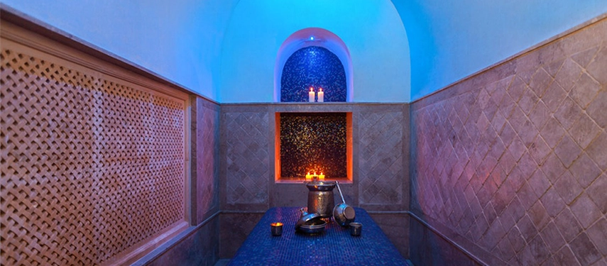 Traditional hammam room with blue mosaic table, candles, and soft glowing light creating a serene spa atmosphere.