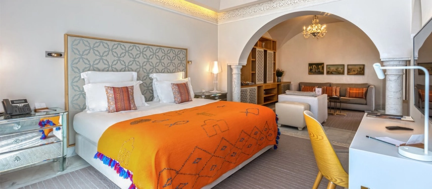 Luxurious suite with king-sized bed, orange throw, and an adjoining lounge beneath decorative arches.
