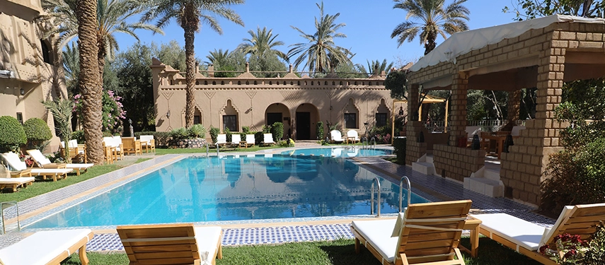 Inviting swimming pool surrounded by palm trees, sun loungers, and kasbah-style walls in the gardens of Ksar El Kabbaba.