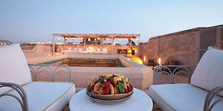 Evening rooftop setting at Dar Bensouda with a fruit platter, pool, and lantern-lit seating area.