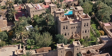 Aerial view of Ksar El Kabbaba showing the kasbah’s towers, lush palm gardens, and central swimming pool courtyard.
