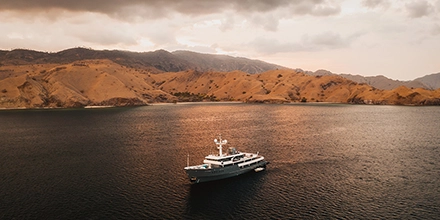 Aqua Blu anchored in a tranquil bay at dusk, surrounded by golden-hued hills under a soft, overcast sky.