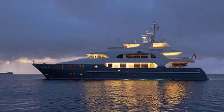 Aqua Mare illuminated against a twilight sea, her elegant profile reflecting warm light onto the still Galápagos waters.