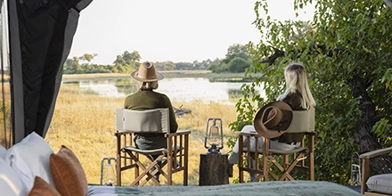 Couple sitting in safari chairs on their private tent veranda with views of the Delta floodplains.