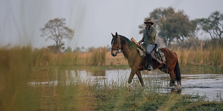 Guide on horseback crossing shallow water during a horse riding safari at Cha Cha Metsi.