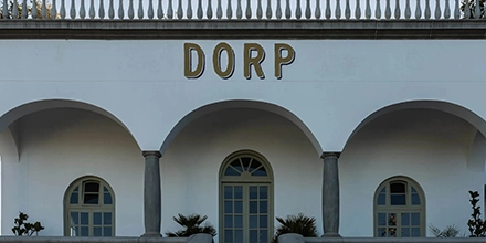 Front façade of Dorp Hotel in Cape Town featuring grand arches, pale walls, and bold gold lettering against a clear sky.