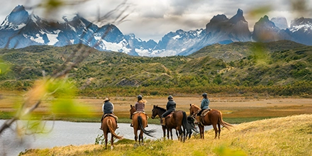 Riders on horseback pause beside a glacial lake, taking in sweeping views of the jagged Torres del Paine peaks.