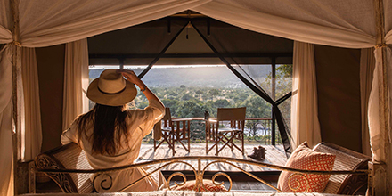 Woman gazes out from a canvas tent at Serian ‘The Original’, looking toward a scenic river view from her bed.