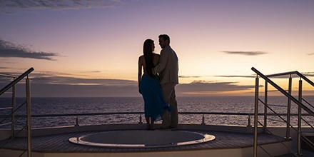 Couple standing beside jacuzzi on the Hermes Galápagos Mega Catamaran’s sun deck at dusk.