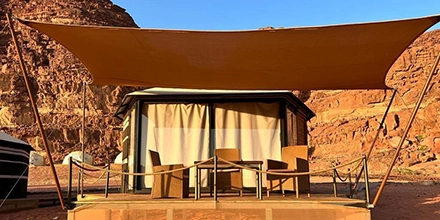 A shaded private terrace fronts a traditional desert tent, framed by sandstone cliffs glowing in the afternoon light.