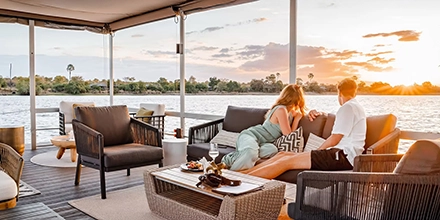 Couple relaxing on a riverside deck watching the sunset over the Zambezi near Insika Lodge, Victoria Falls.