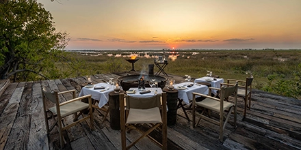 Open-air dining platform at the Zarafa Dhow Suite in the Selinda Reserve, arranged for a private safari dinner as the sun sets over the plains.