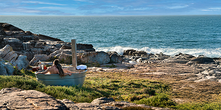 A person enjoying an outdoor hot tub by the ocean at sunset.