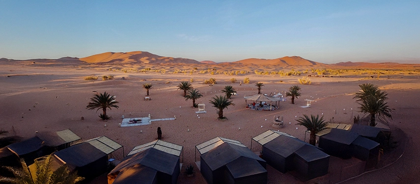 Expansive desert landscape with Riad Madu camp tents and dunes glowing in the morning light.
