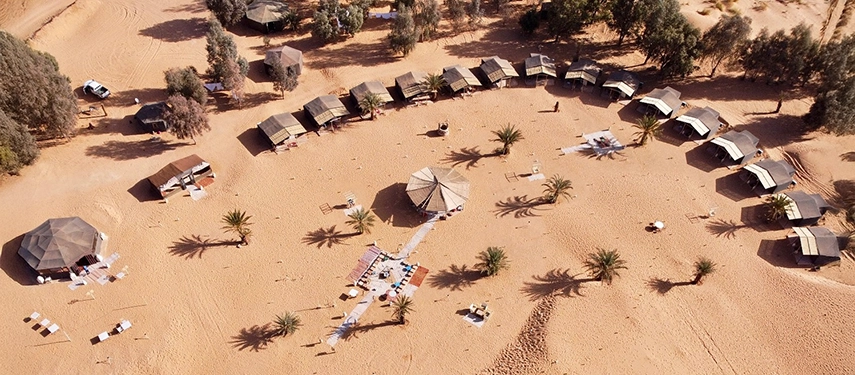 Aerial view of Riad Madu Luxury Desert Camp with tents arranged in a semi-circle on the sand.