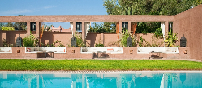 Swimming pool bordered by green lawn and shaded lounge alcoves with Moroccan lanterns.