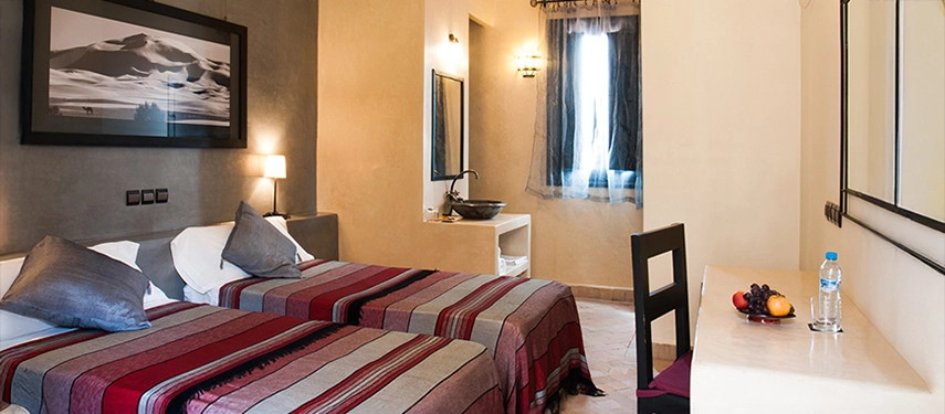 Twin room with striped red and grey bedding, modern furnishings, and a window letting in soft natural light.