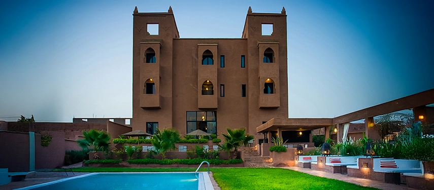 Dar Chamaa’s illuminated façade at dusk with pool and garden in the foreground.