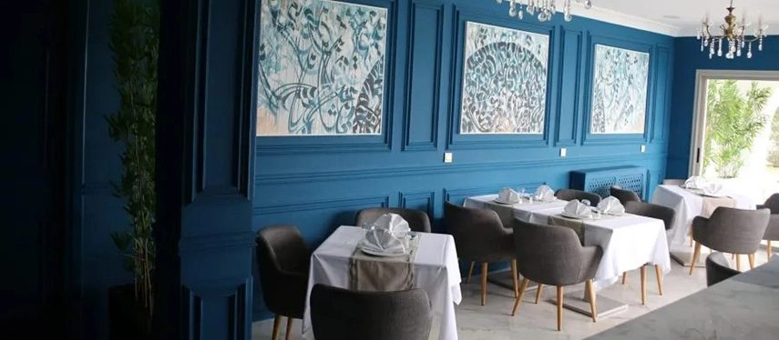 Stylish dining room with deep blue walls, modern furnishings, and artwork with Arabic calligraphy.