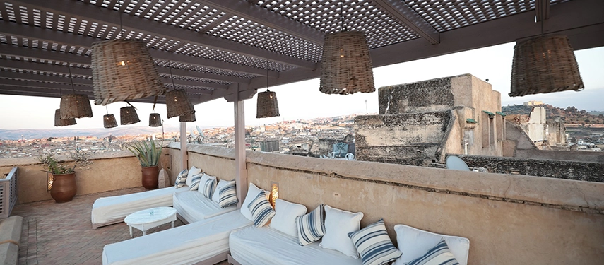 Covered rooftop lounge at Dar Bensouda with striped cushions and views across the Fes medina.