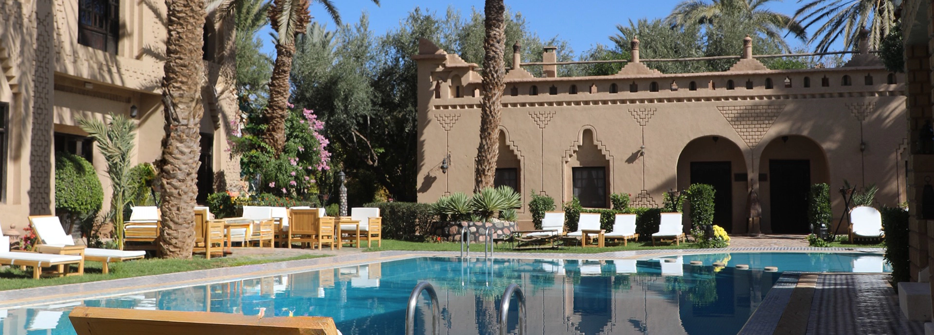Shimmering turquoise swimming pool framed by palm trees and kasbah walls at Ksar El Kabbaba.