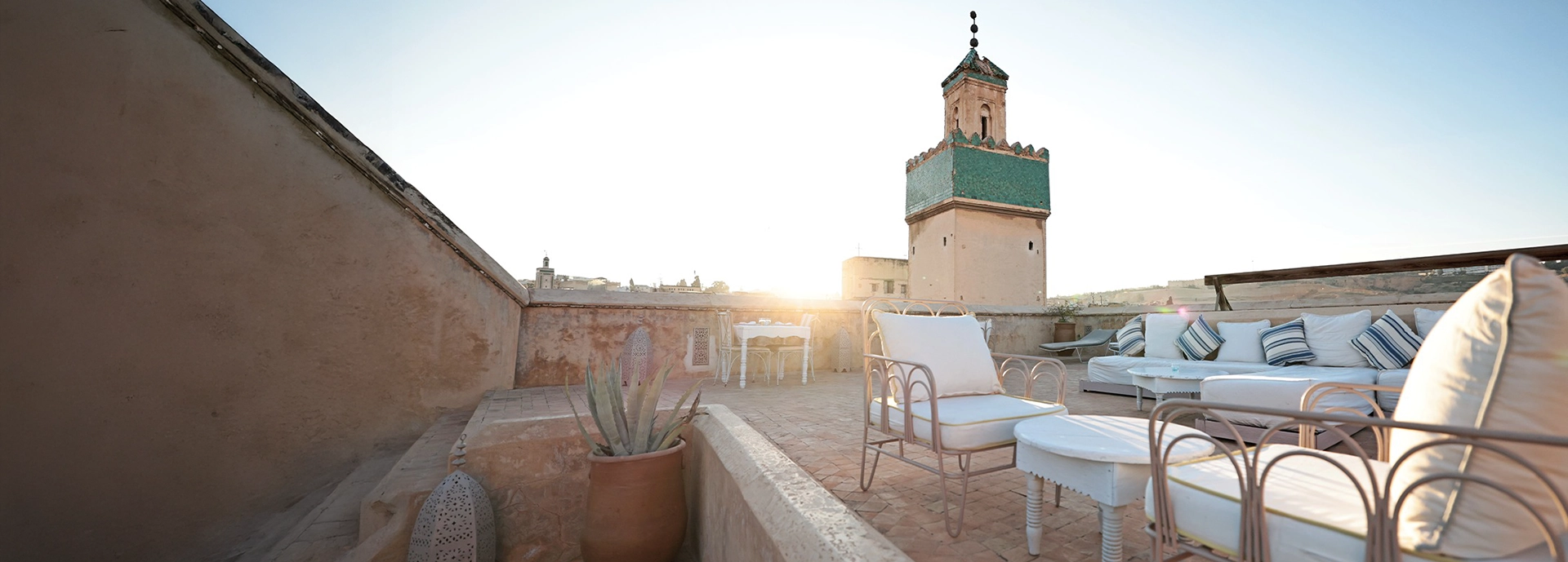 Rooftop terrace at Dar Bensouda with cushioned lounge seating and views of a green-tiled minaret at sunrise.