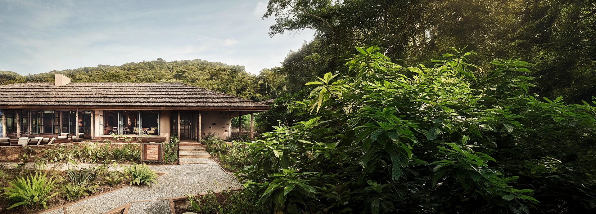 Wide-angle view of the main Gorilla Forest Lodge surrounded by lush greenery, showcasing its eco-conscious design and integration with the forest.