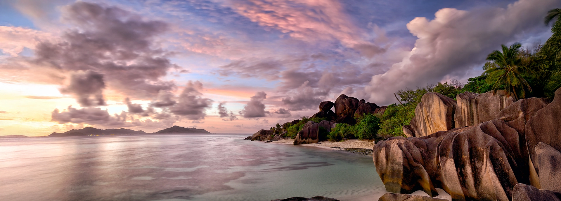 Sunset over granite boulders and tranquil turquoise waters in the Seychelles.