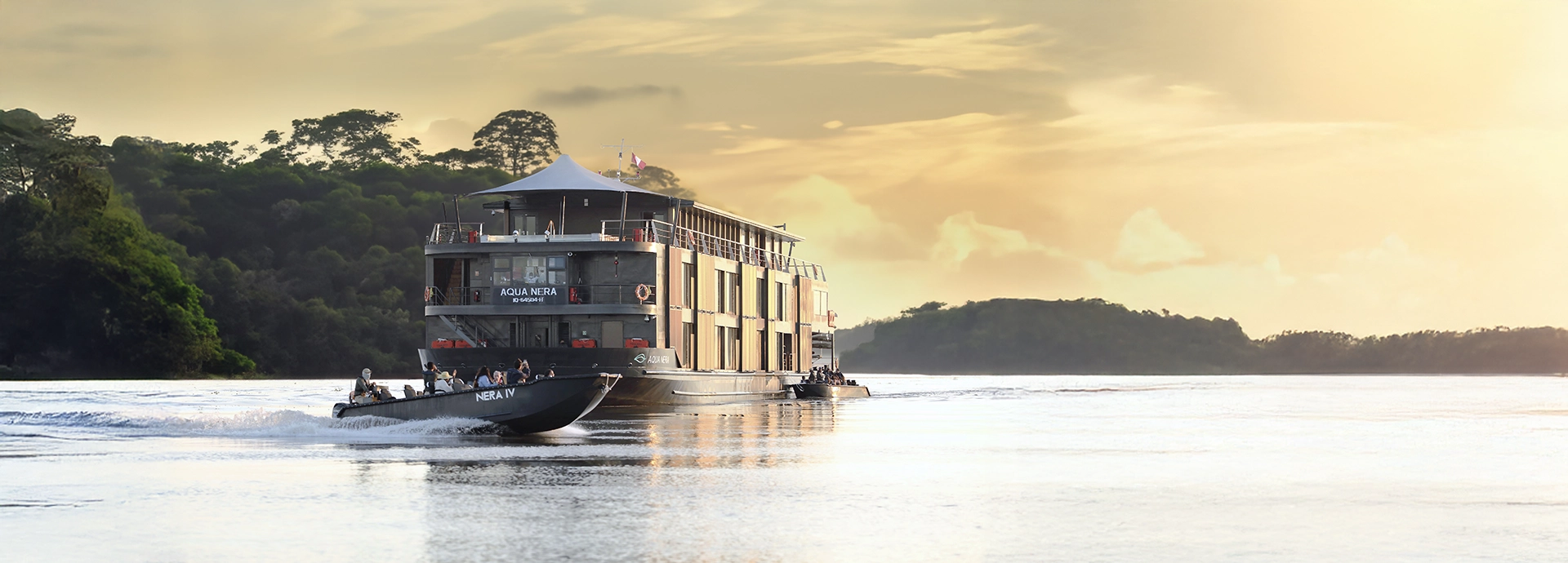 Aqua Nera cruising the Amazon at sunrise, with a skiff of guests exploring beside it against a backdrop of misty forest.